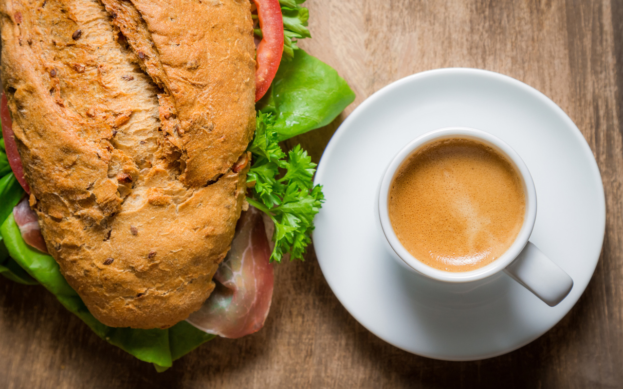 Чашка кофе с бутербродом на столе к завтраку 