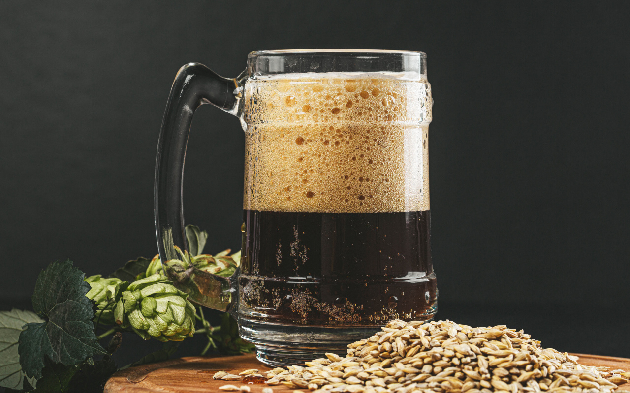 Темное пиво в бокале на столе с хмелем и зернами пшеницы 