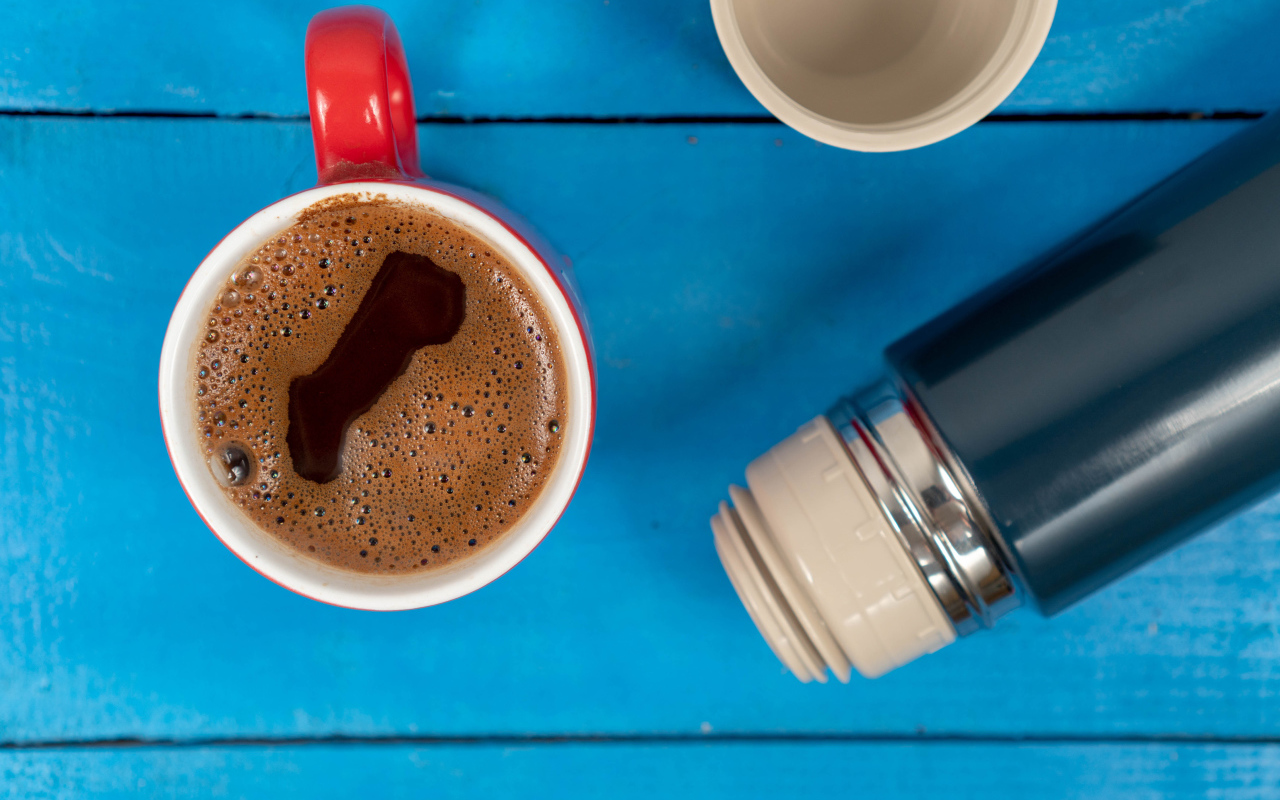 Красная чашка кофе с термосом на голубом столе 