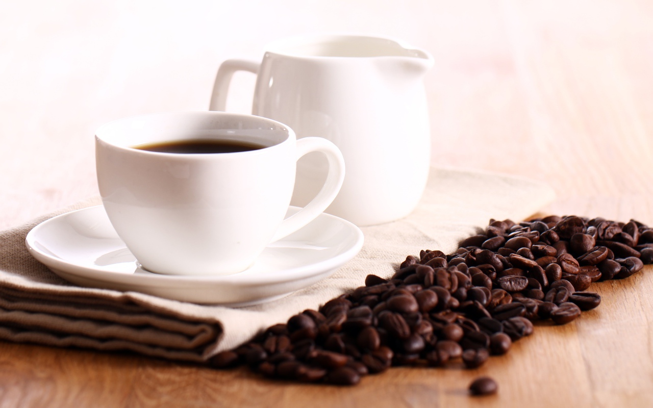 Белая чашка кофе на столе с молоком и зернами