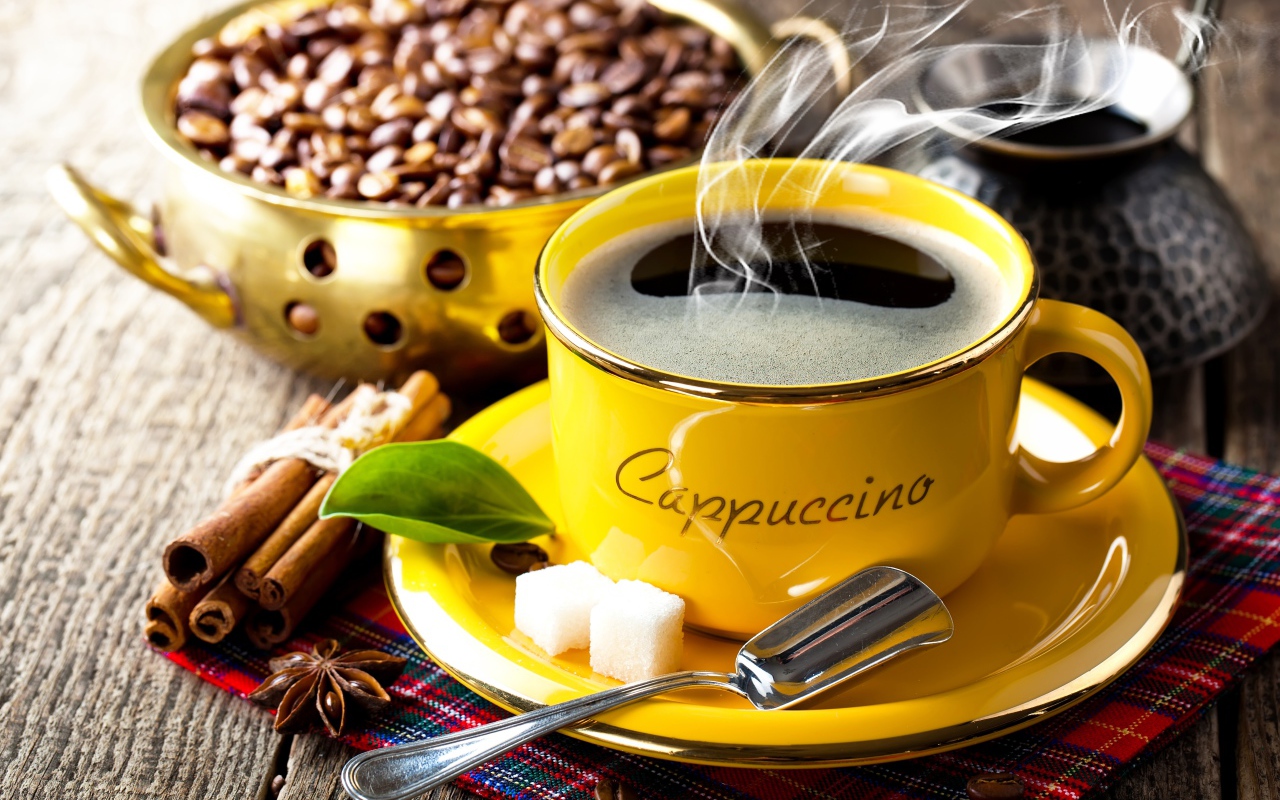 Желтая чашка с горячим кофе на столе с зернами и корицей 