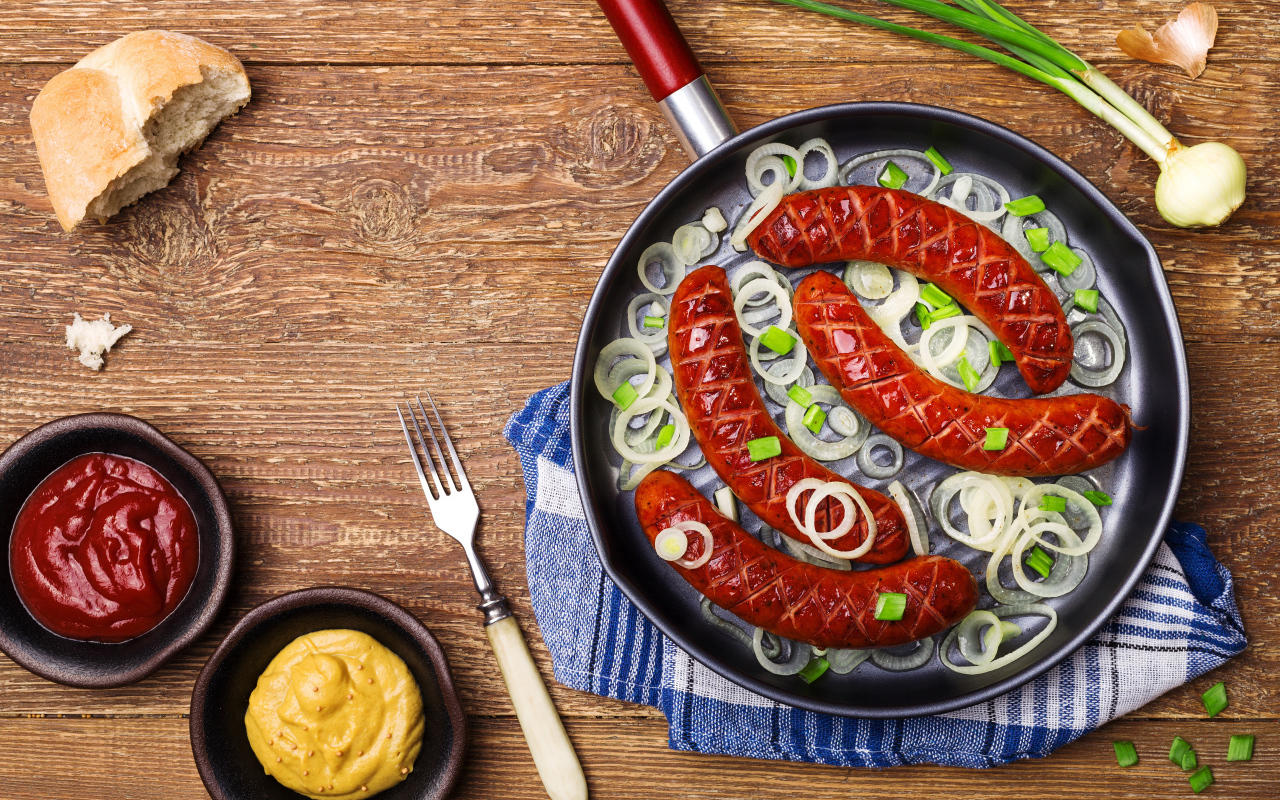 Колбаски барбекю с луком на сковороде на столе с соусом