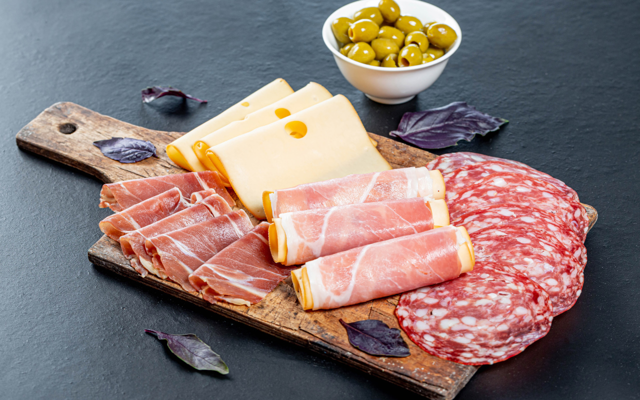 Сыр, бекон и колбаса на разделочной доске на столе с оливками