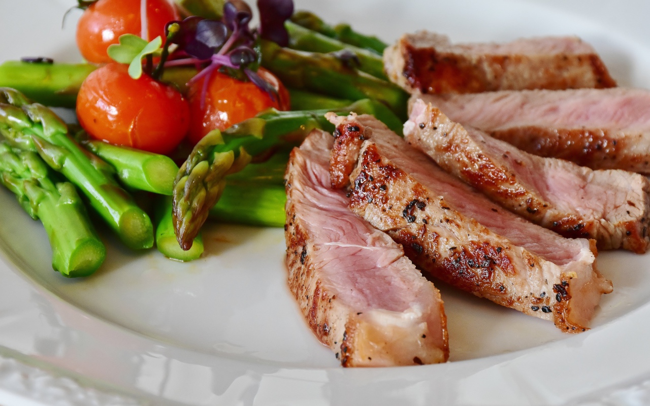 Chunks of meat on a plate with asparagus and tomatoes
