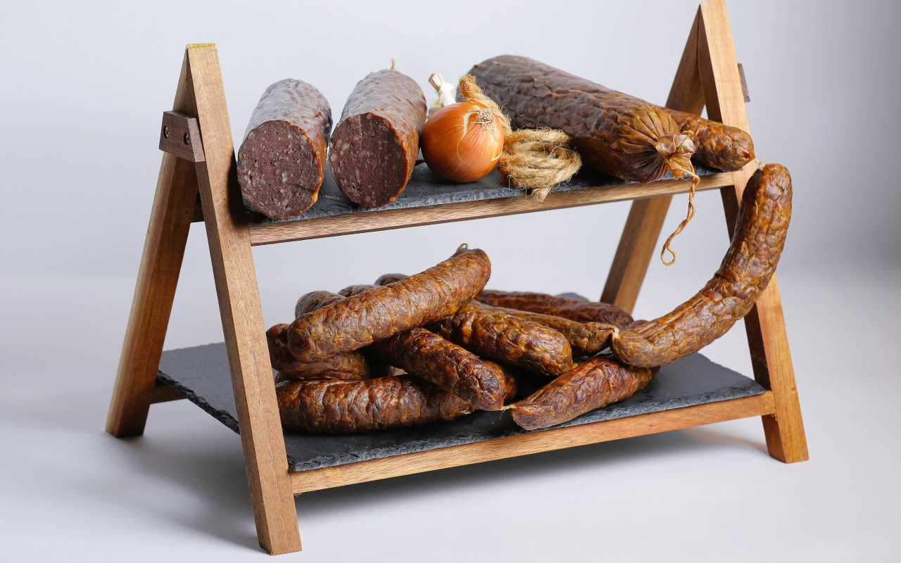 Различные виды колбасы на полке с луком на сером фоне
