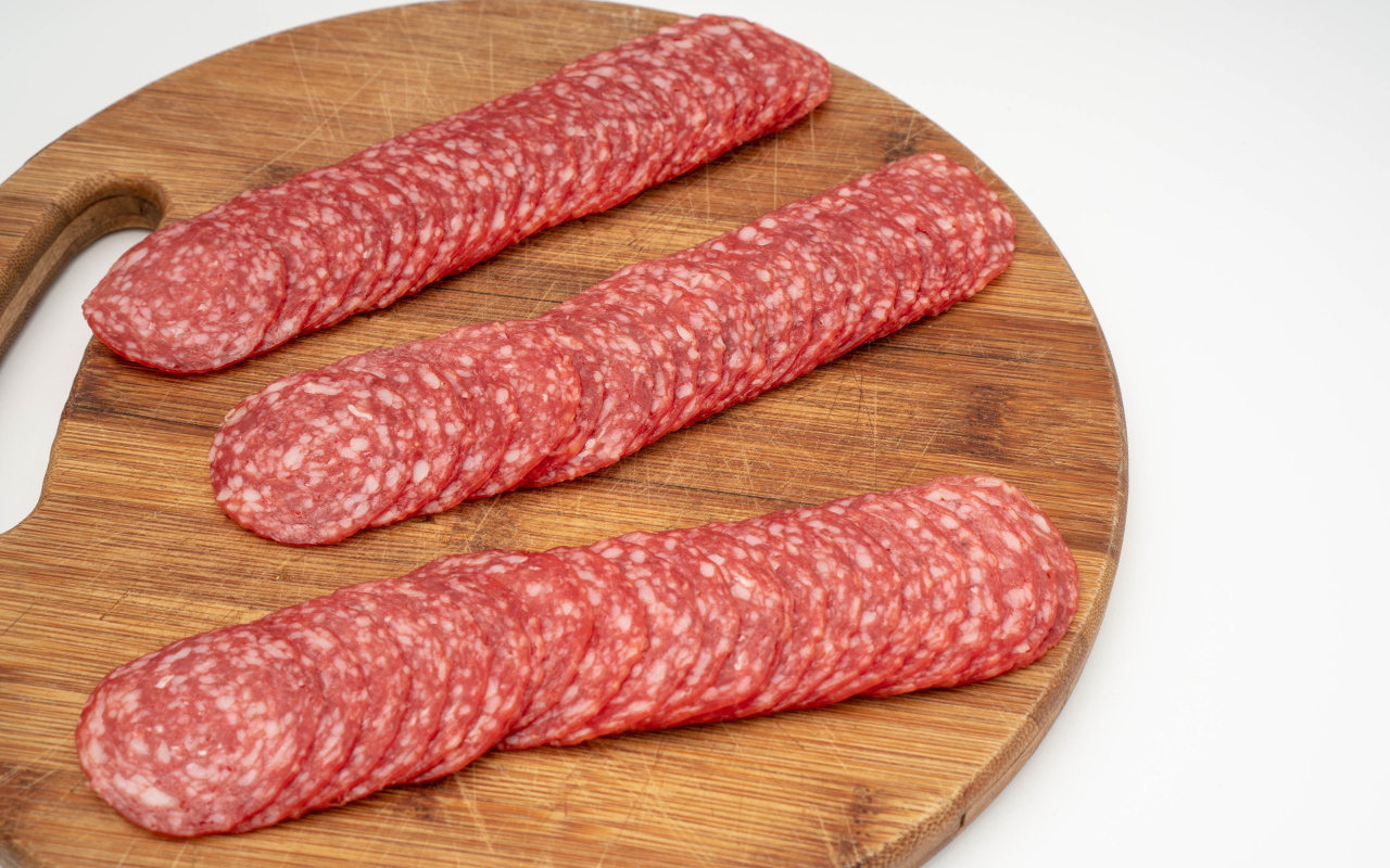 Колбаса тонко нарезана на разделочной доске 