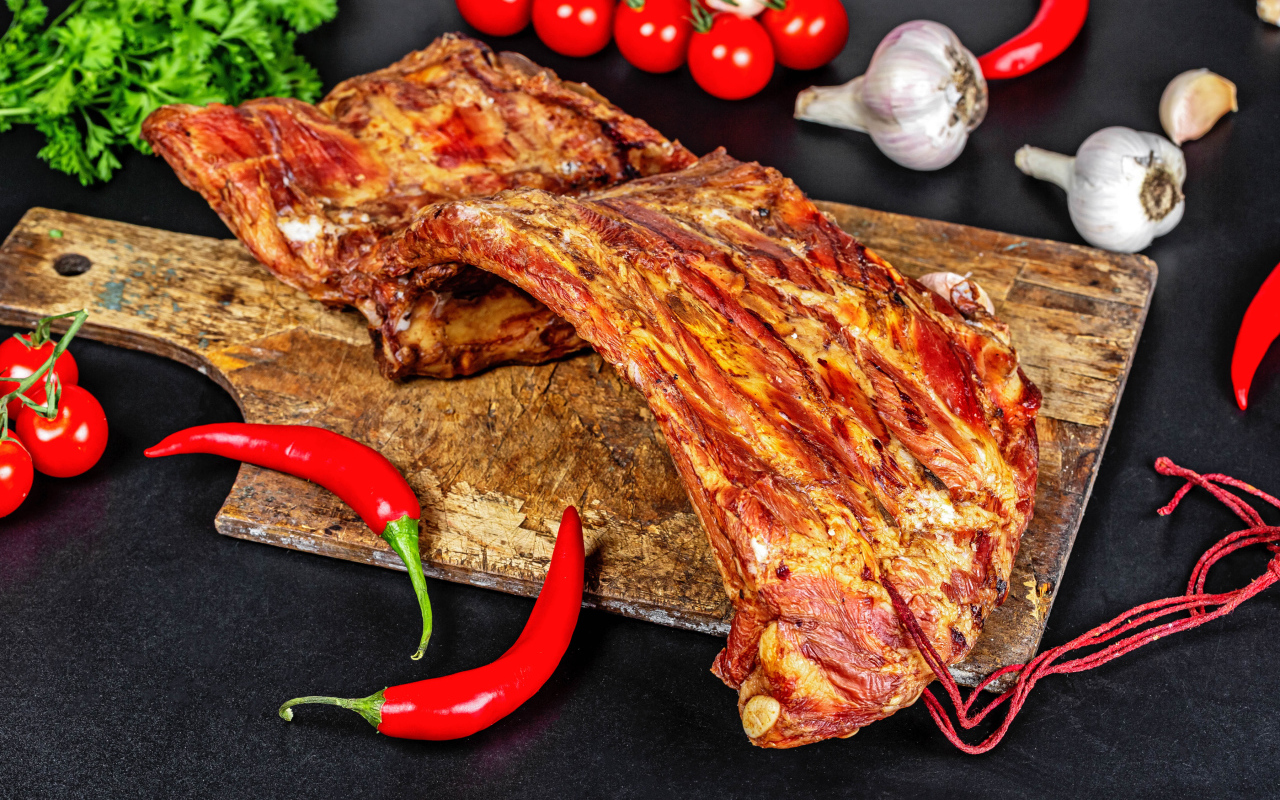 Копченые ребра на столе с красным перцем, чесноком и помидорами