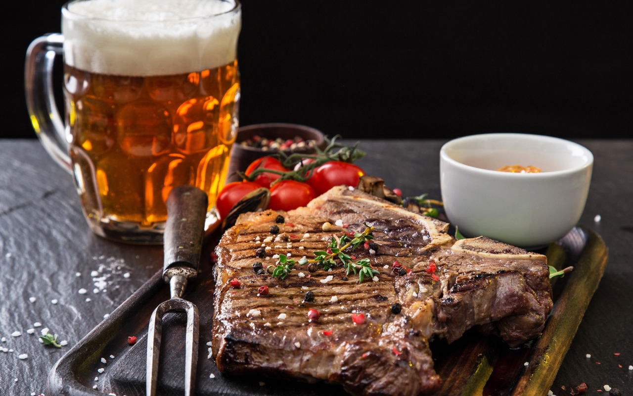 Вкусный кусок мяса на столе с помидорами и бокалом пива