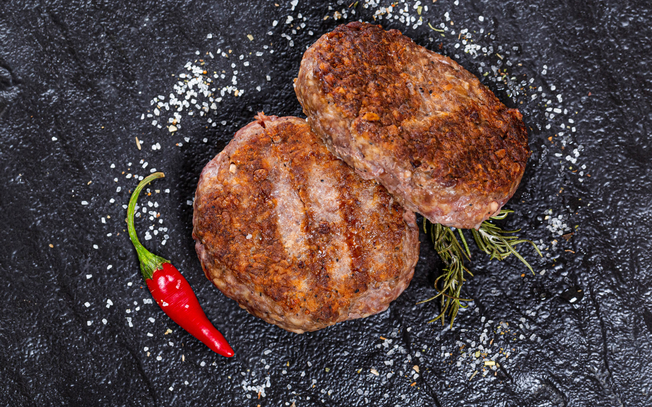 Две котлеты на черной поверхности с красным перцем