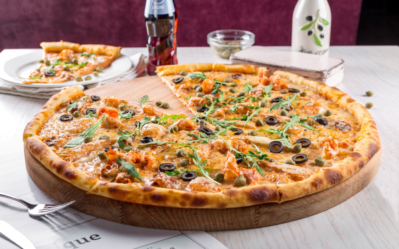 Большая аппетитная пицца с маслинами на столе в кафе