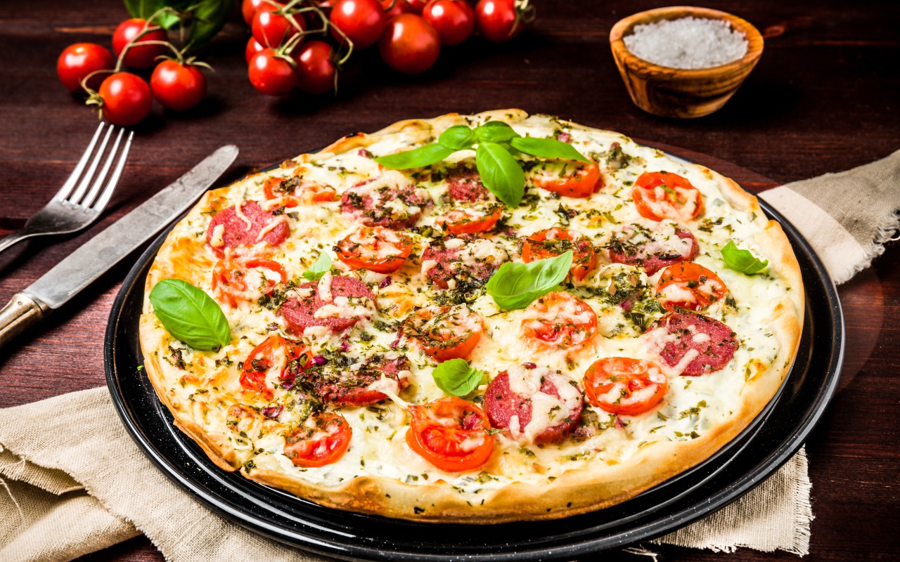 Вкусная пицца с колбасой, сыром и помидорами на столе 