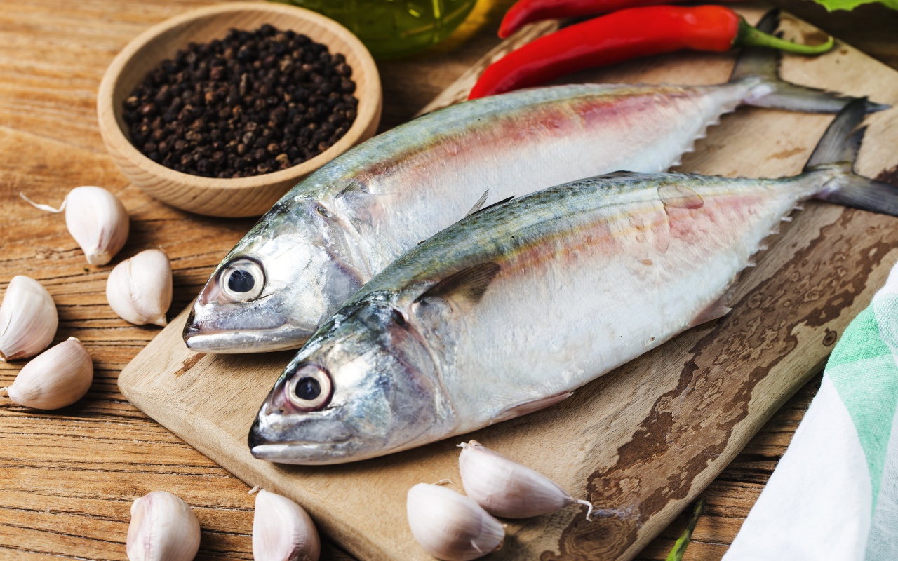 Свежая рыба лежит на доске с чесноком и специями