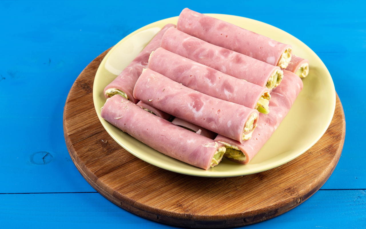 Рулетики из ветчины на тарелке на голубом столе