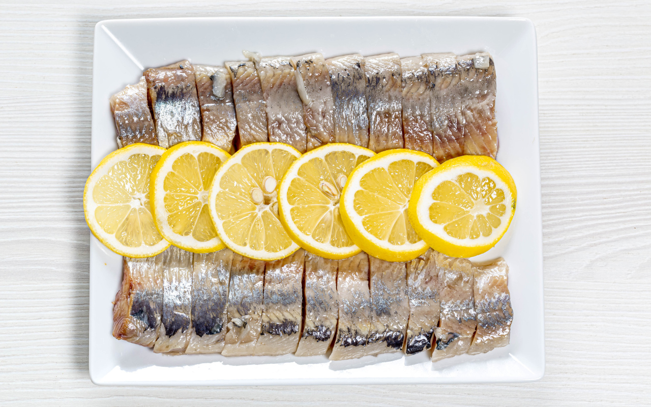 Селедка нарезанная кусочками на белой тарелке с лимоном 