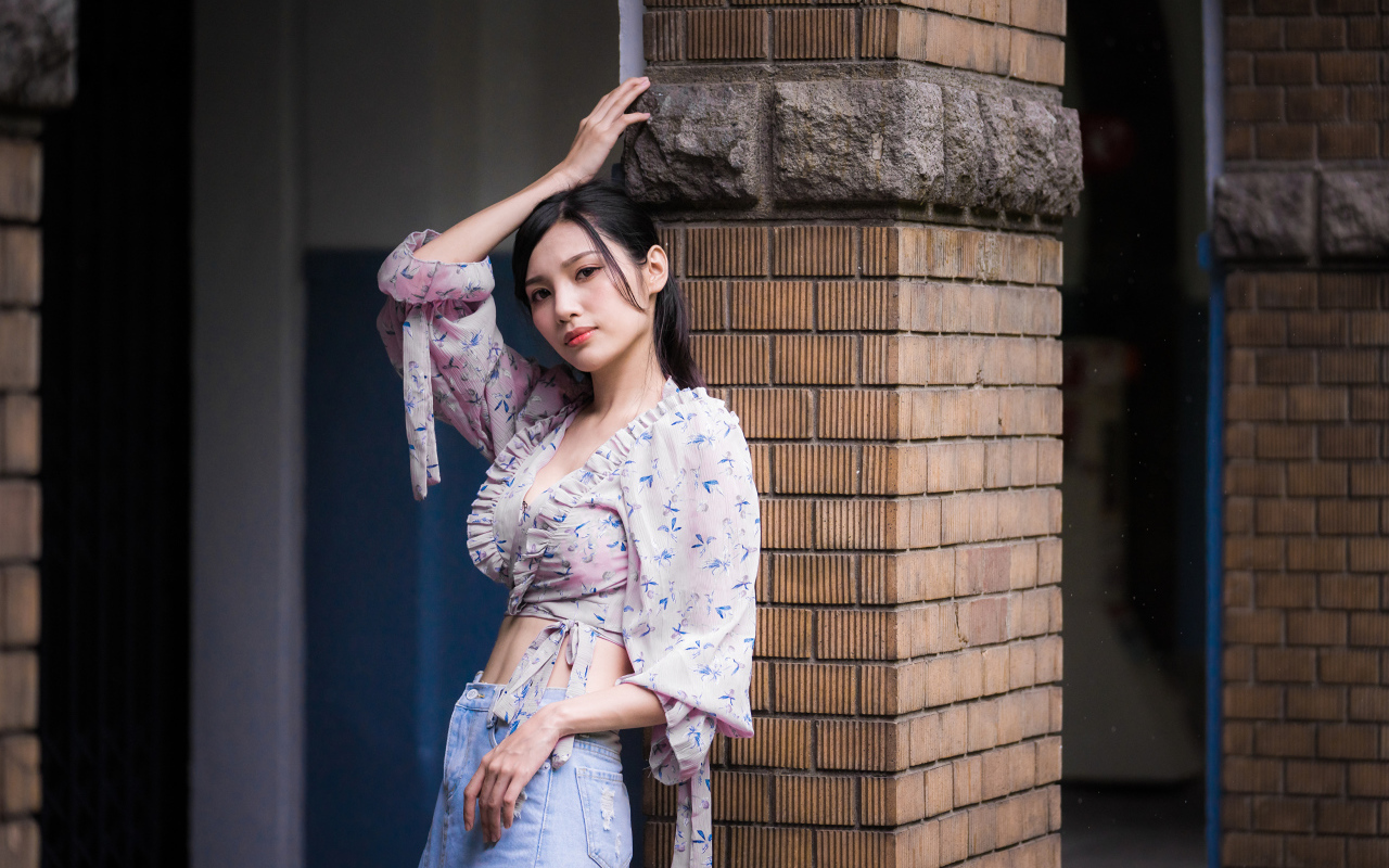 Красивая девушка азиатка стоит у кирпичной колонны 