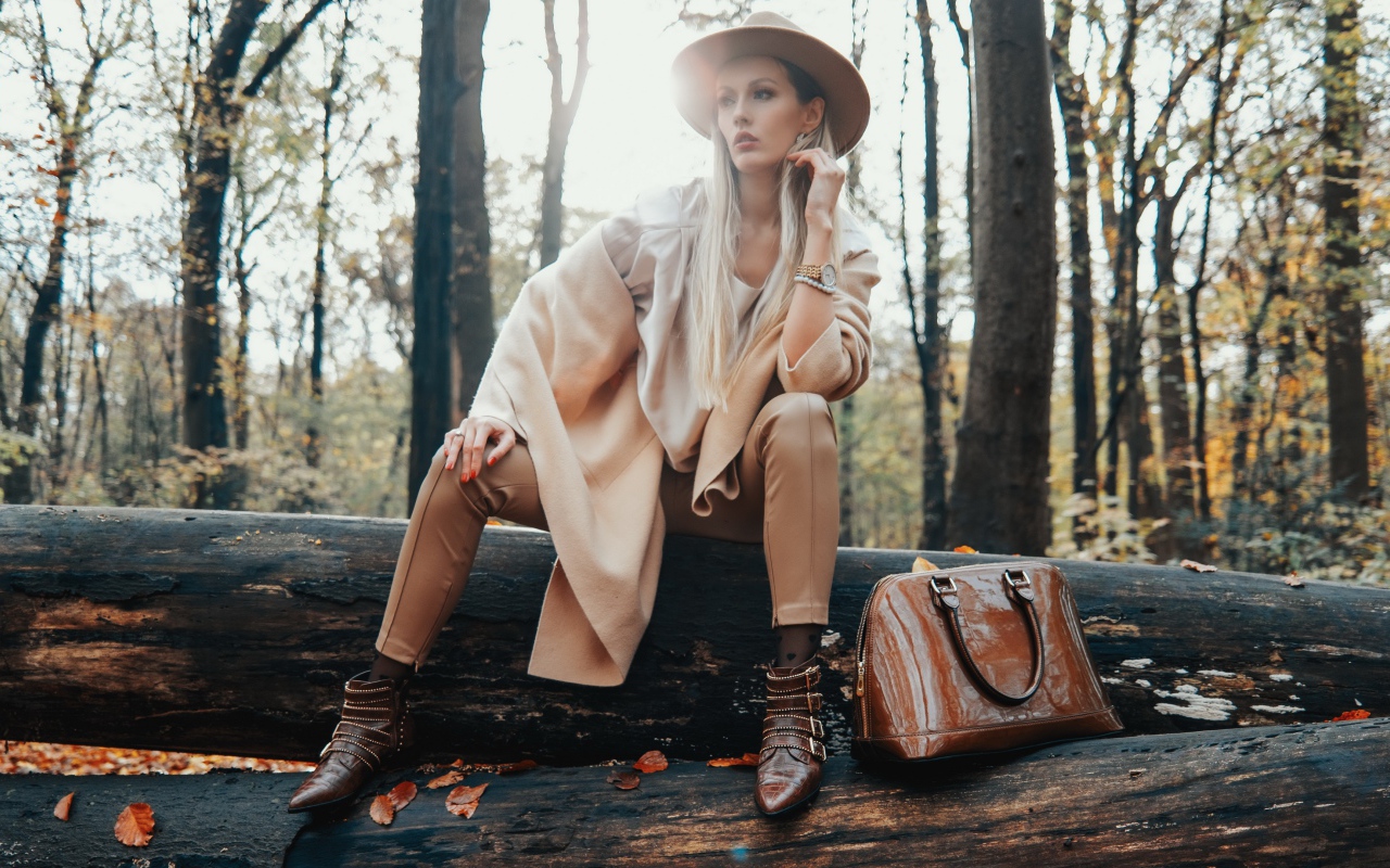 Девушка в пальто сидит на упавшем дереве в лесу 