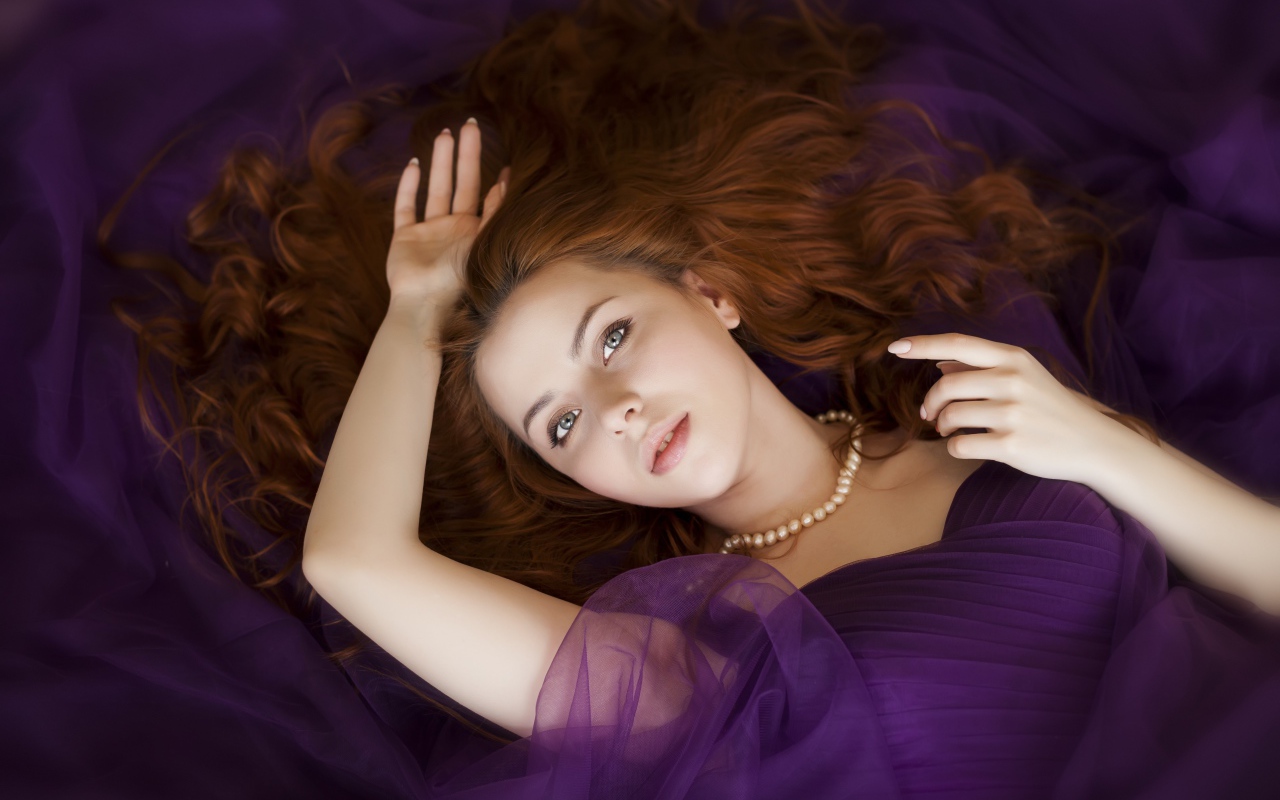 Рыжеволосая девушка в фиолетовом наряде лежит на полу