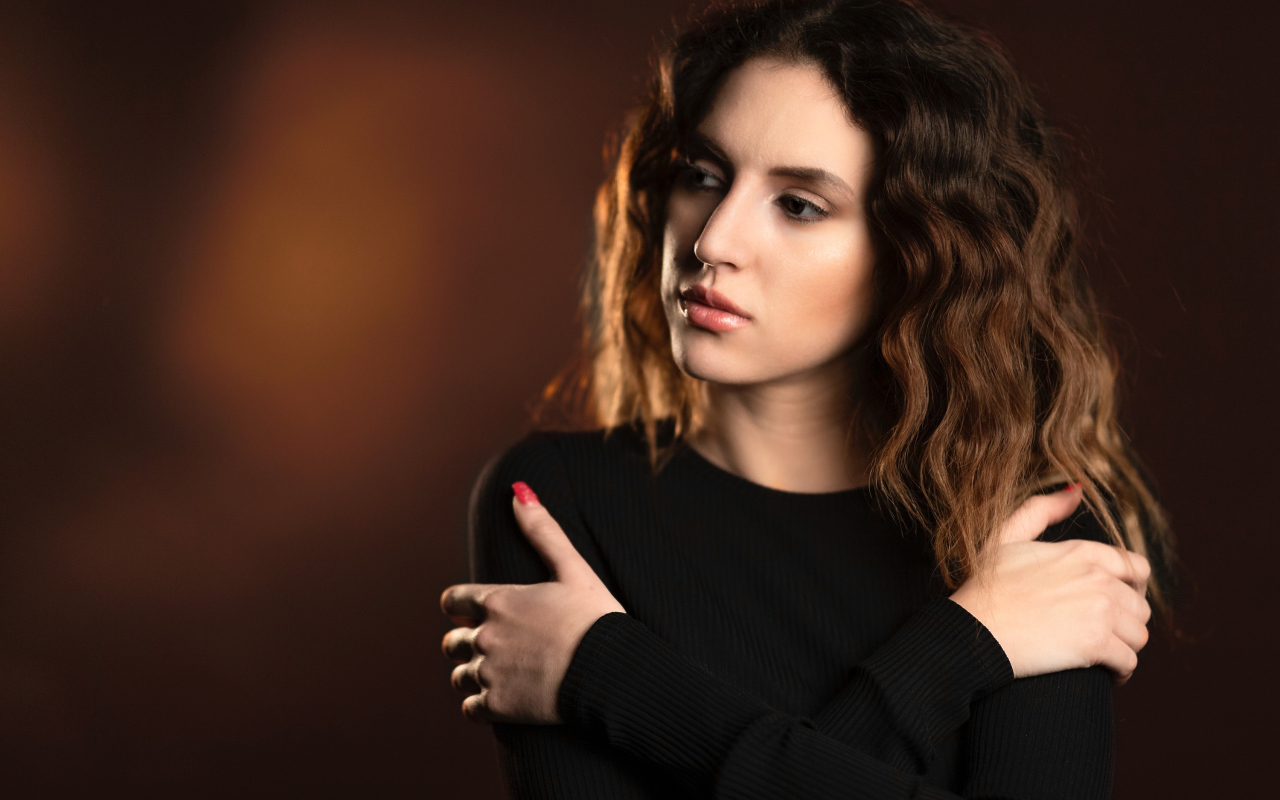 Молодая девушка стоит у стены в черном свитере