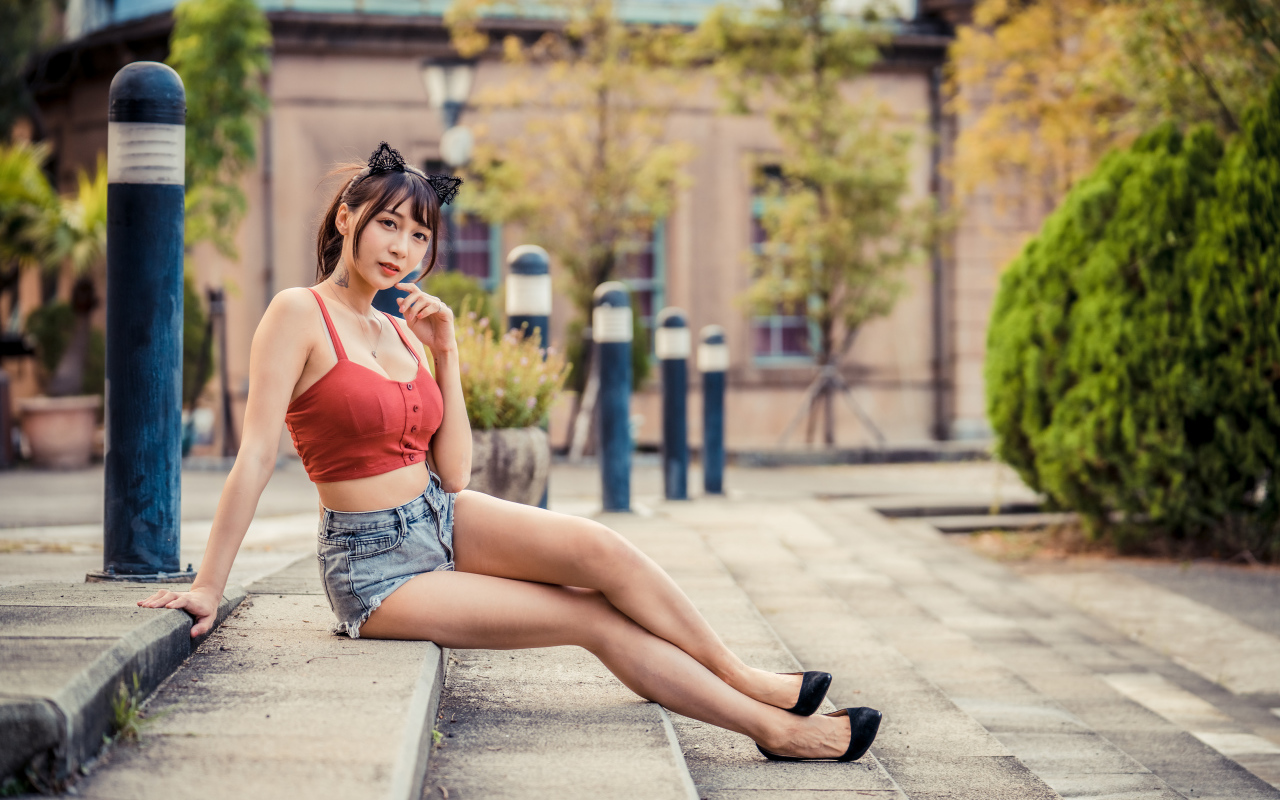 Азиатка в шортах сидит на ступенях 