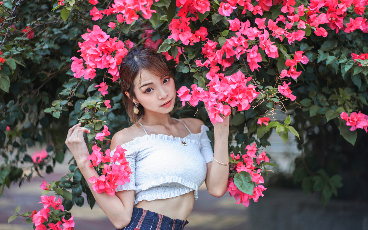 Красивая азиатка стоит у дерева с красными цветами