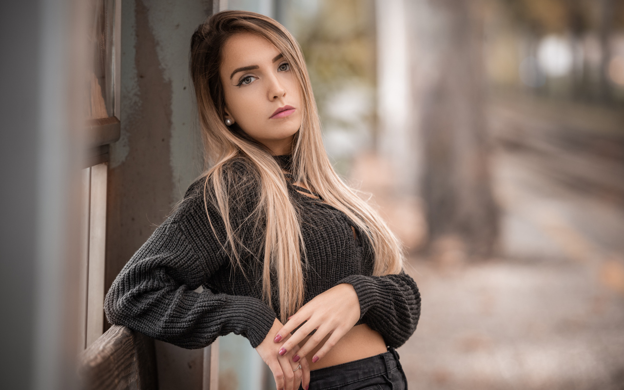Красивая блондинка в вязаном свитере у стены 