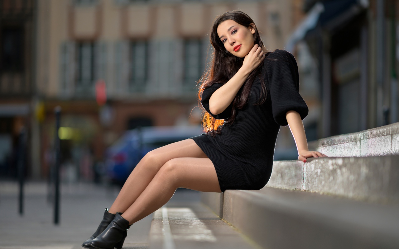 Красивая девушка в черном платье сидит на ступенях