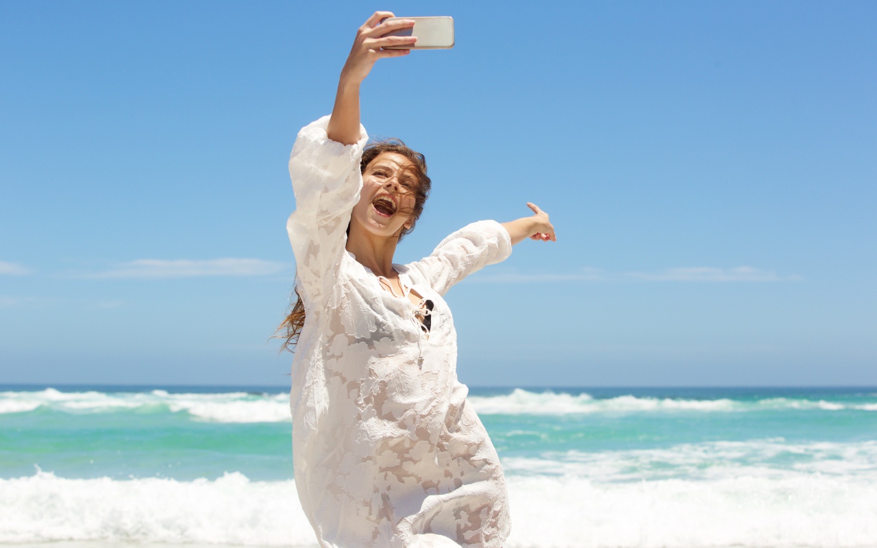 Красивая девушка в белом платье делает селфи на море 