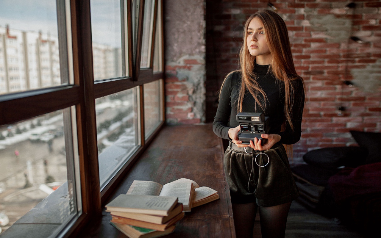 Красивая девушка с фотоаппаратом в руках у окна 