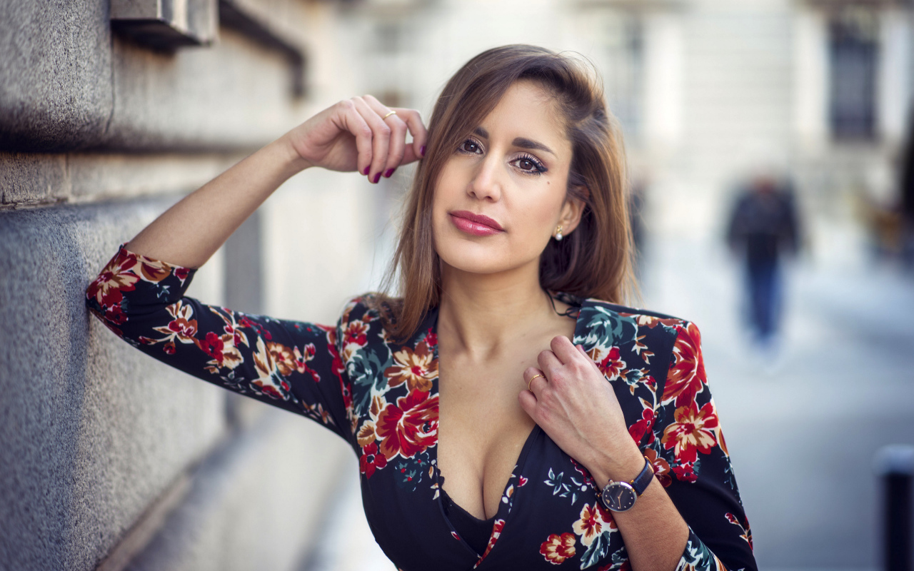 Красивая девушка с часами на руке стоит у стены