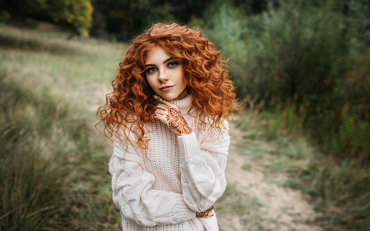 Красивая рыжеволосая девушка в белом свитере с рисунками из хны на руках