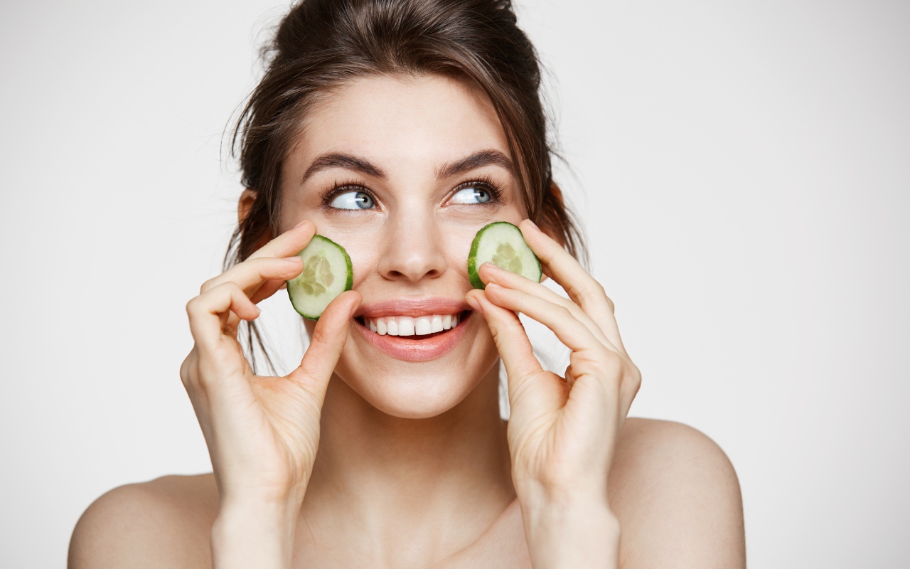 Голубоглазая девушка прикладывает огурцы к лицу 