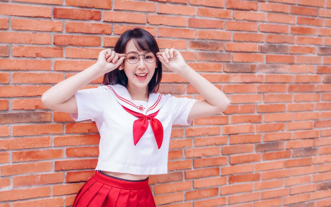 Яркая веселая азиатка в очках у кирпичной стены