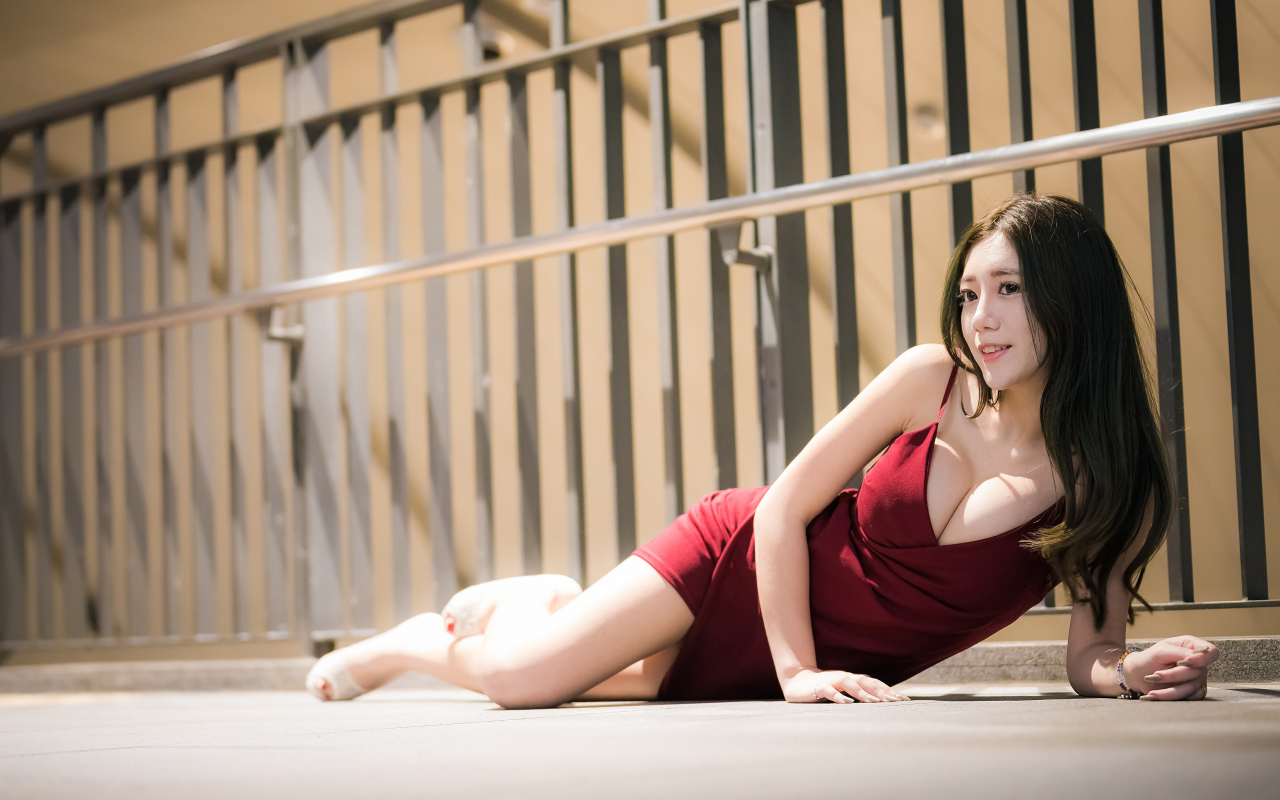 Милая девушка азиатка в красном платье лежит на земле