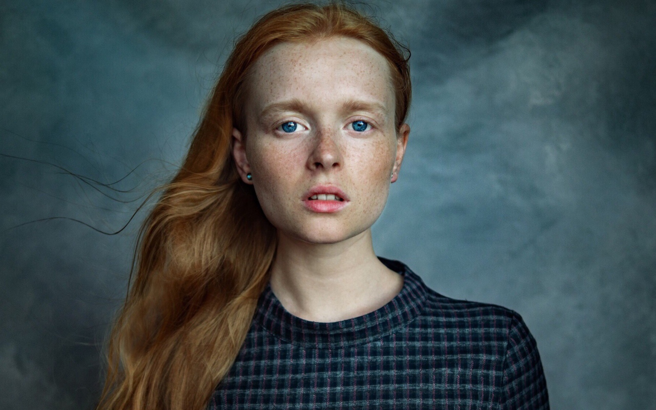 Милая рыжеволосая голубоглазая девушка с веснушками на лице на сером фоне