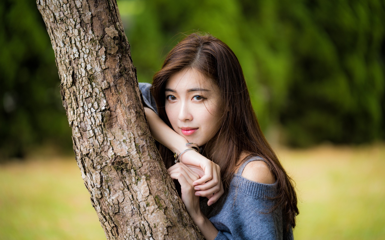 Мечтательная девушка азиатка стоит у дерева