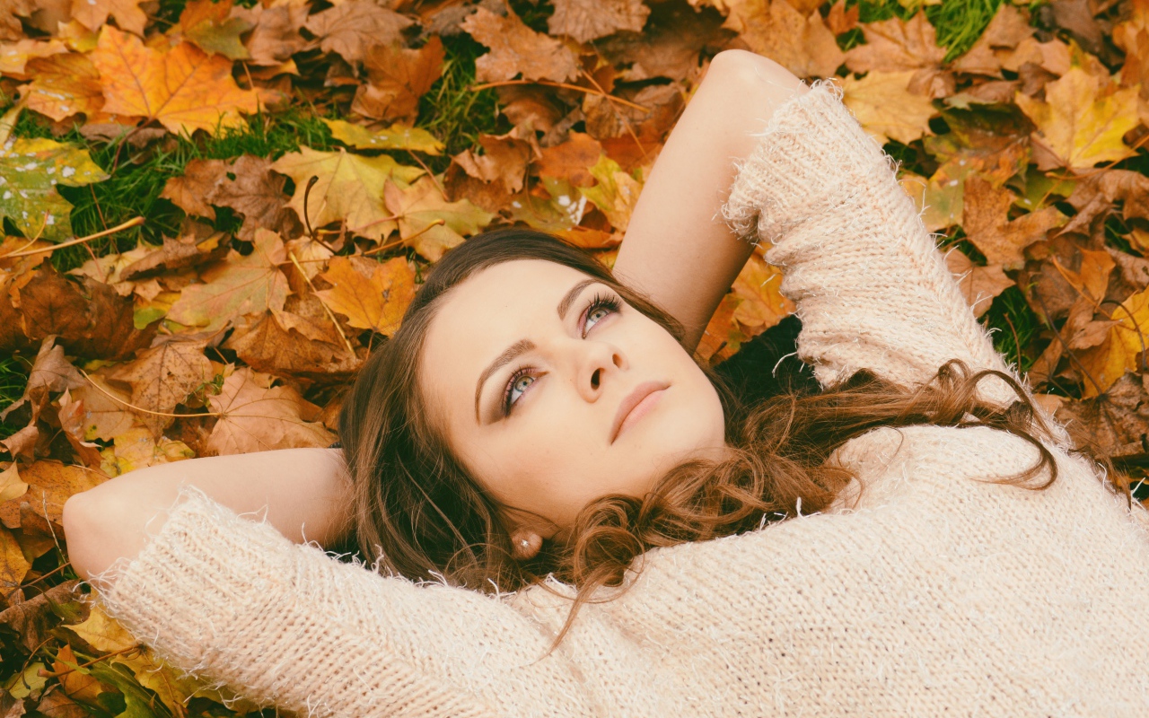 Мечтательная девушка в свитере лежит на земле