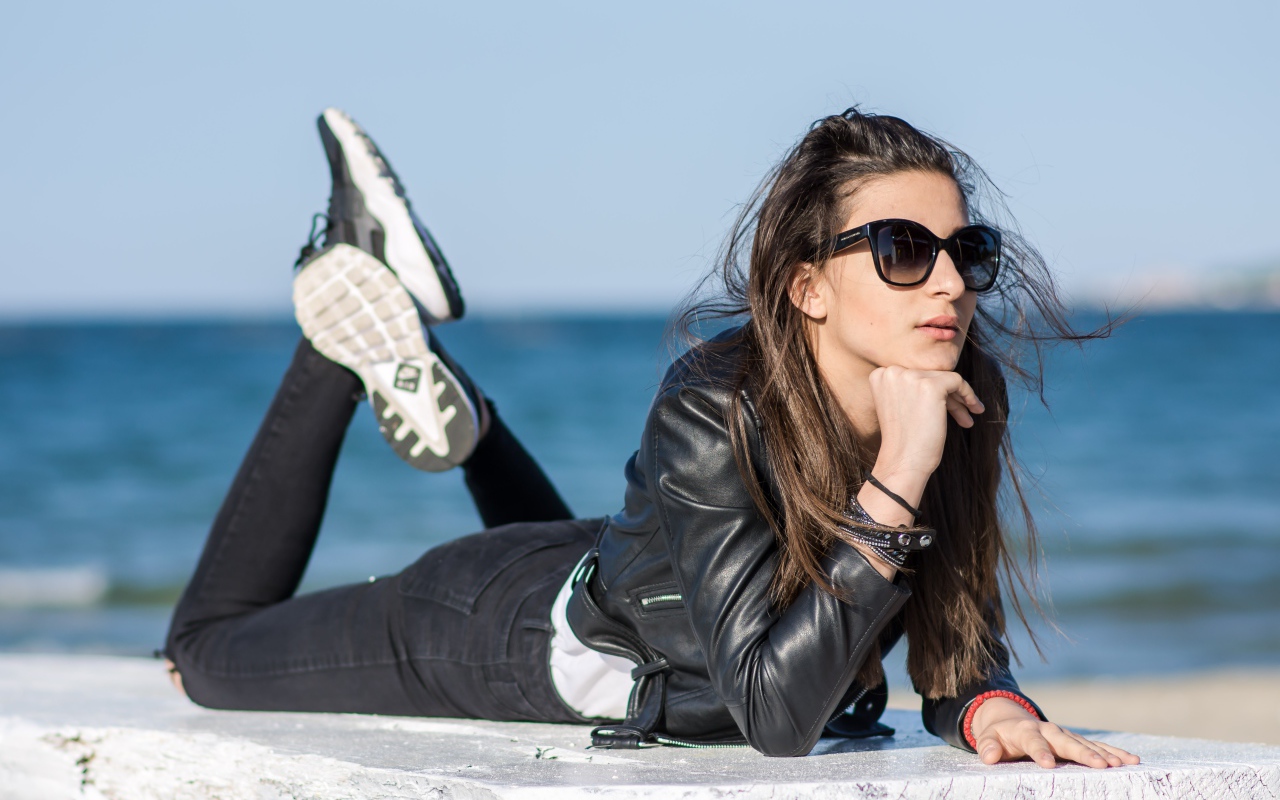 Девушка в черных очках и кожаной куртке на фоне моря