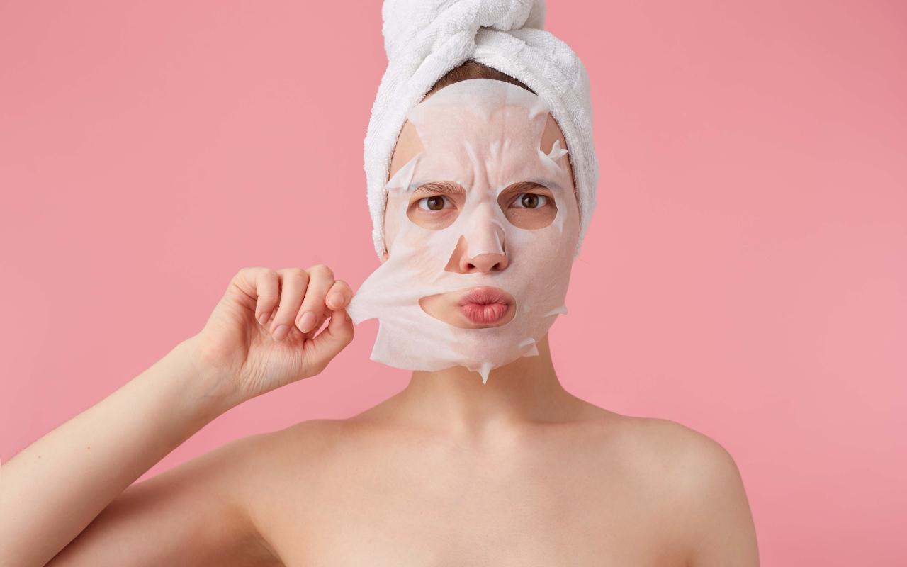 Девушка снимает косметическую маску с лица на розовом фоне 