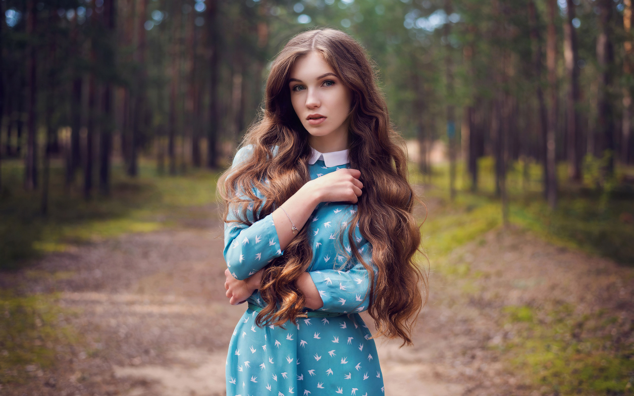 Длинноволосая девушка в голубом платье стоит в лесу
