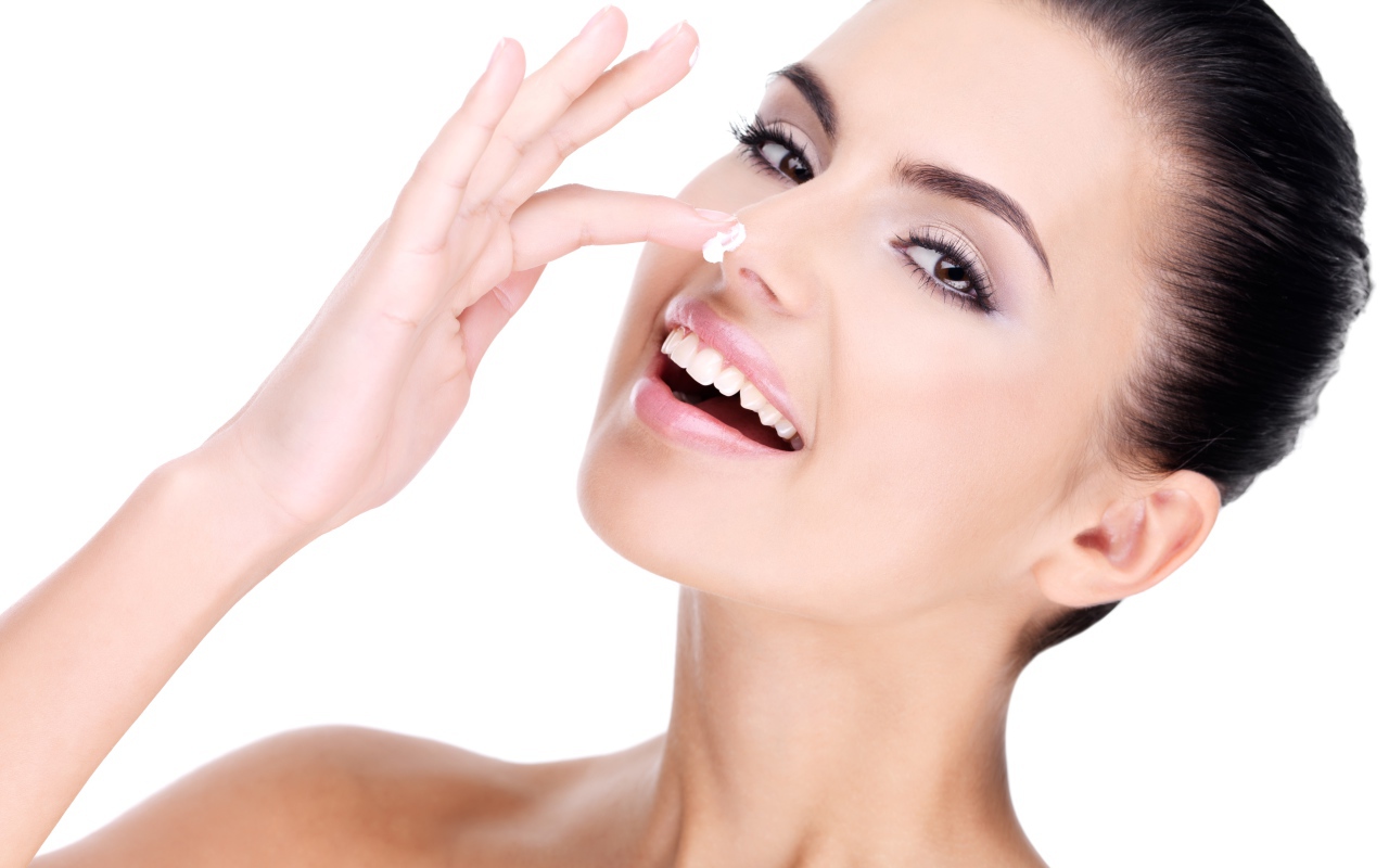 Улыбающаяся девушка мажет крем на нос 