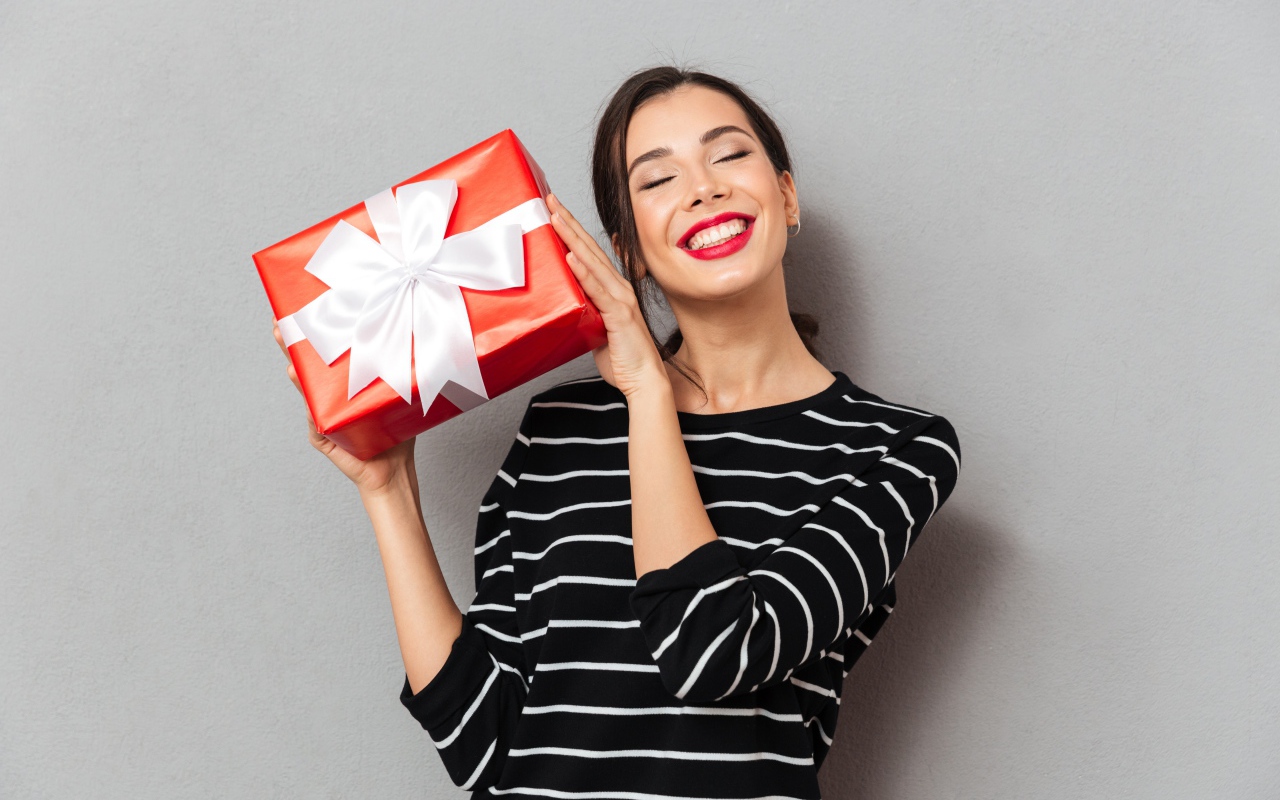 Улыбающаяся девушка с подарком в руках на сером фоне 