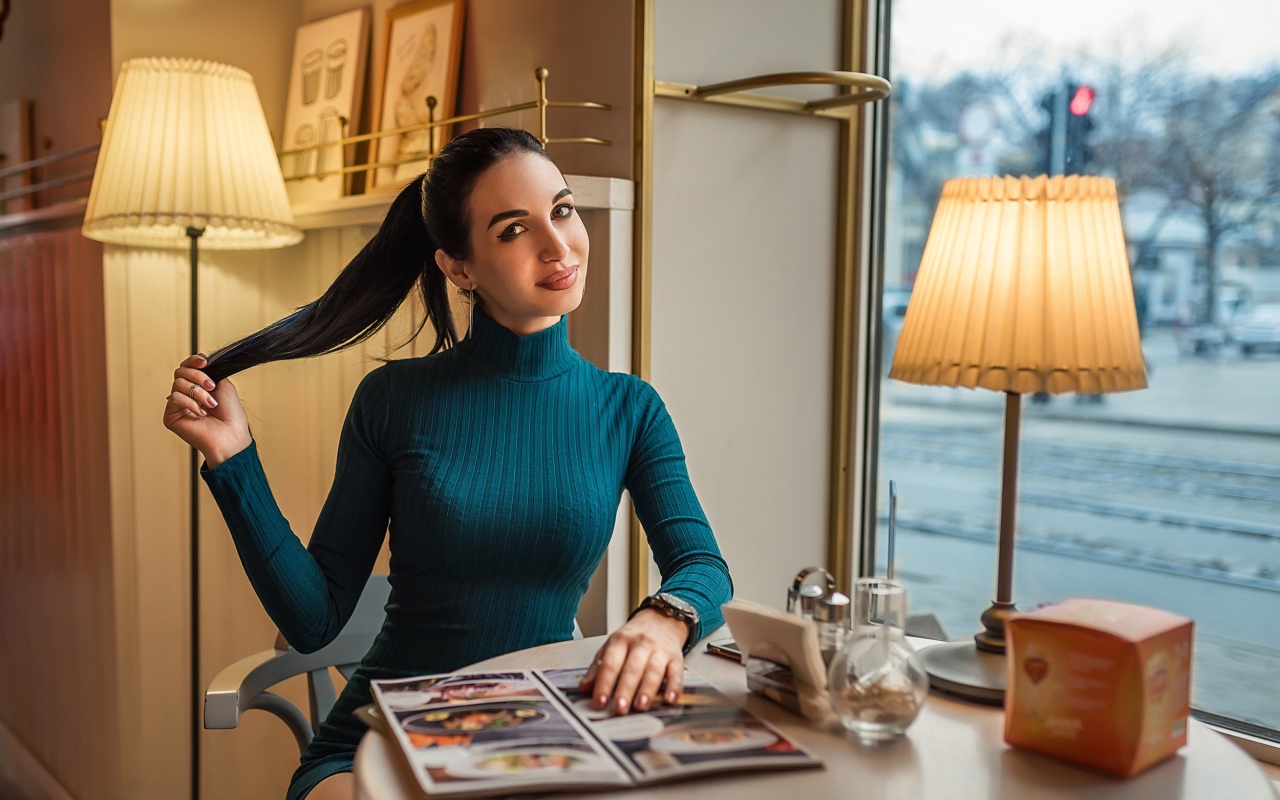 Стильная девушка в платье сидит в кафе у окна