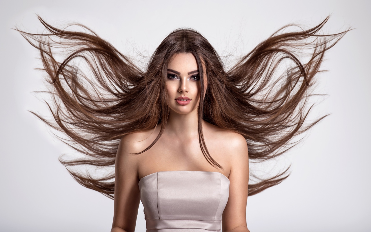 Ветер развивает волосы красивой девушке шатенке на сером фоне