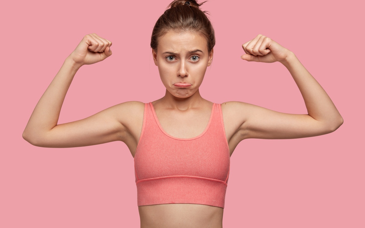 Расстроенная девушка без накаченных рук на розовом фоне