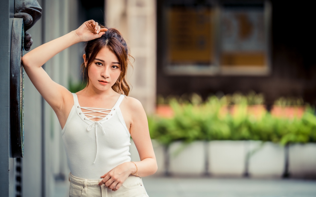 Молодая красивая азиатка в белой майке стоит у ворот