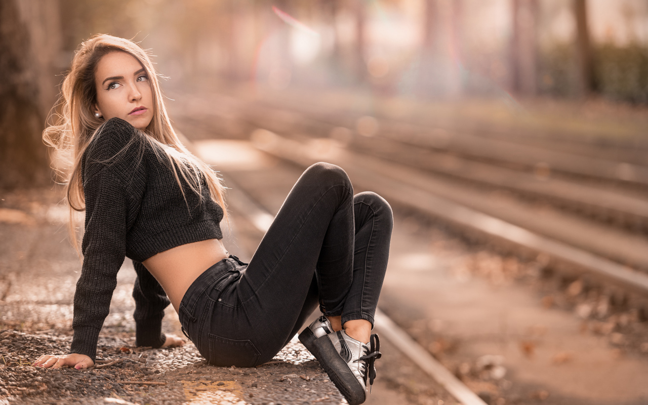 Молодая девушка в джинсах сидит у железной дороги 