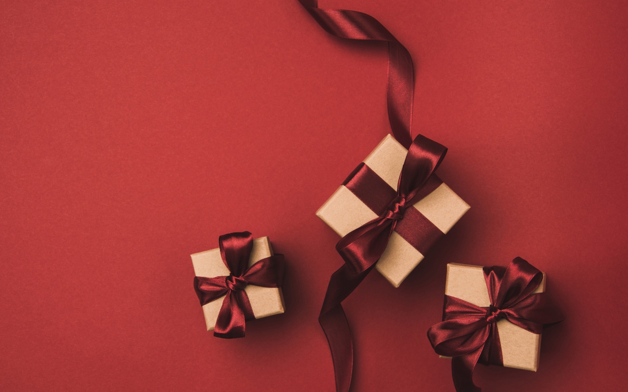 Три подарочные коробки с бантами на красном фоне