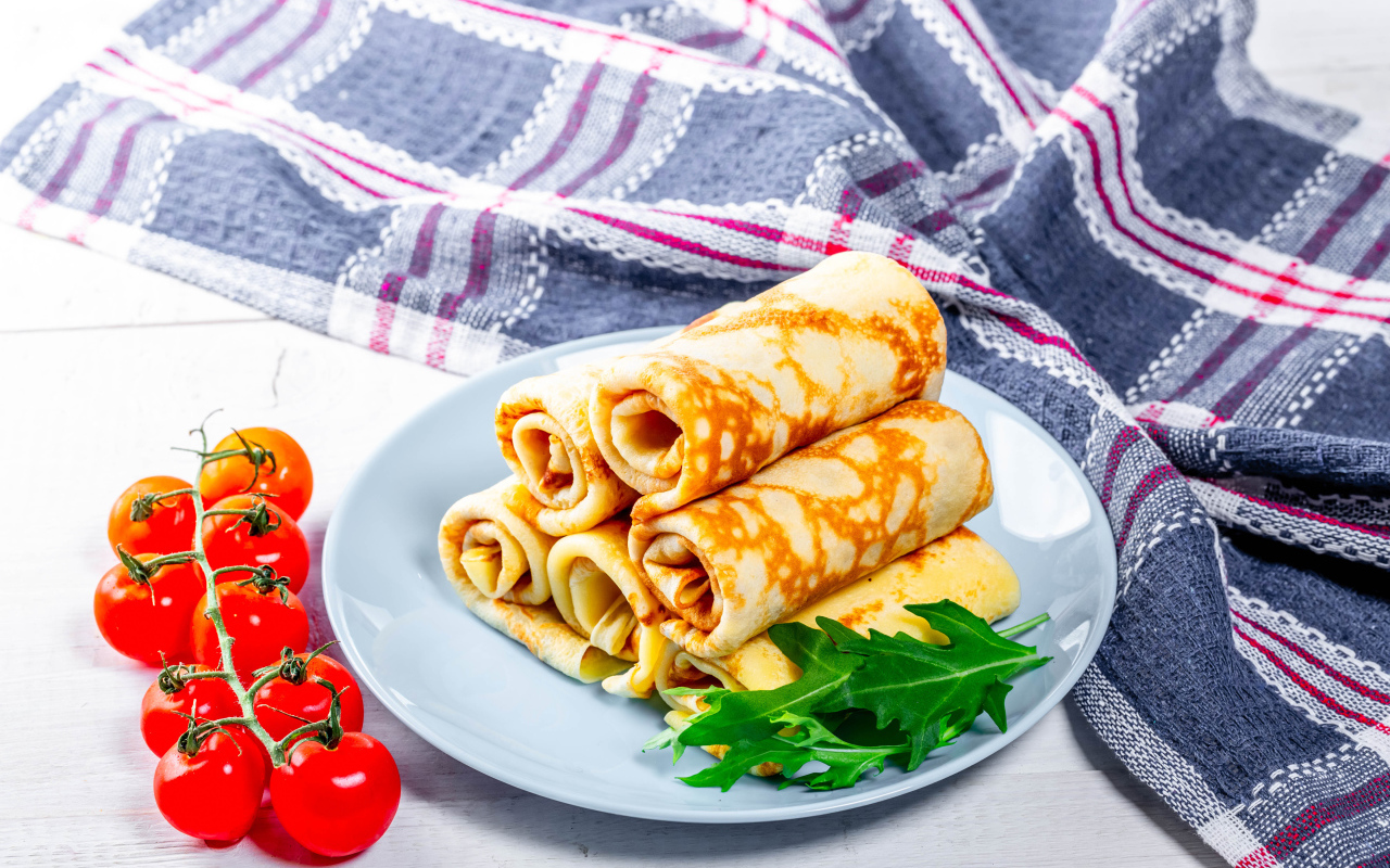 Блинчики на столе с помидорами и полотенцем угощение на Масленицу 2020