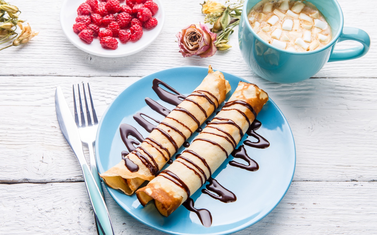 Тонкие блины с шоколадом на столе с ягодами малины и какао 