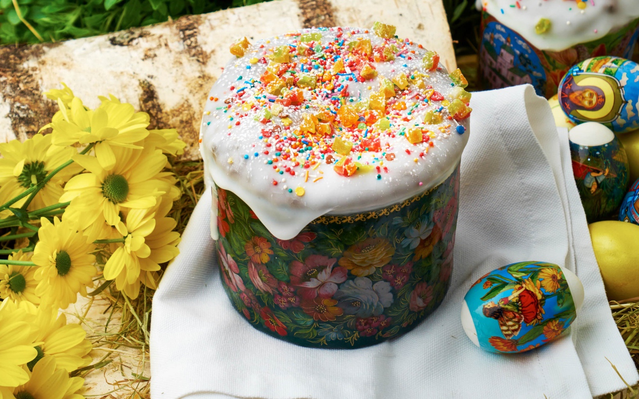 Кулич с глазурью на столе с цветами и яйцами на Пасху